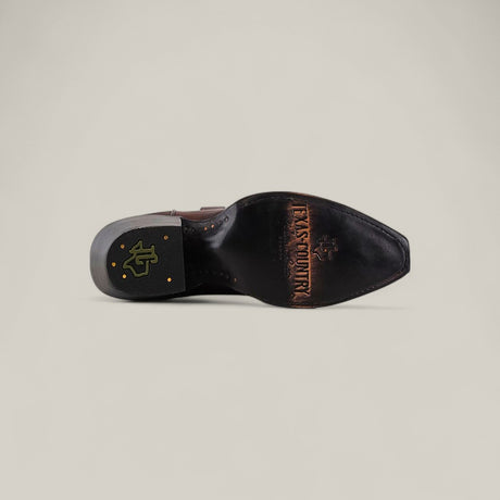 The Miranda Clayton Brownie Leather Sole boot features a TEXAS COUNTRY engraving and cross logo on the sole, plus a black and gold heel emblem—ideal for fans of classic, mid-shaft, snip-toe leather sole boots.