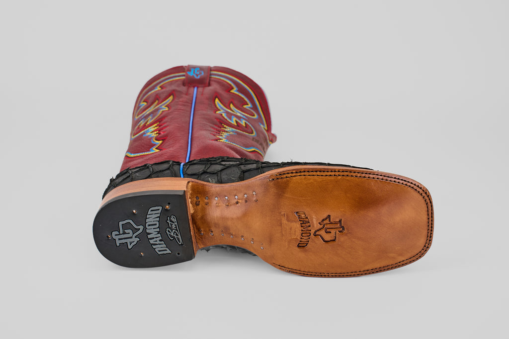 A pair of Dodge - Matte Black - Square Toe boots, one upright and one on its side to display the sole. The matte black boots feature colorful stitching, Pirarucu leather accents, and a leather sole stamped with DIAMOND and the logo.