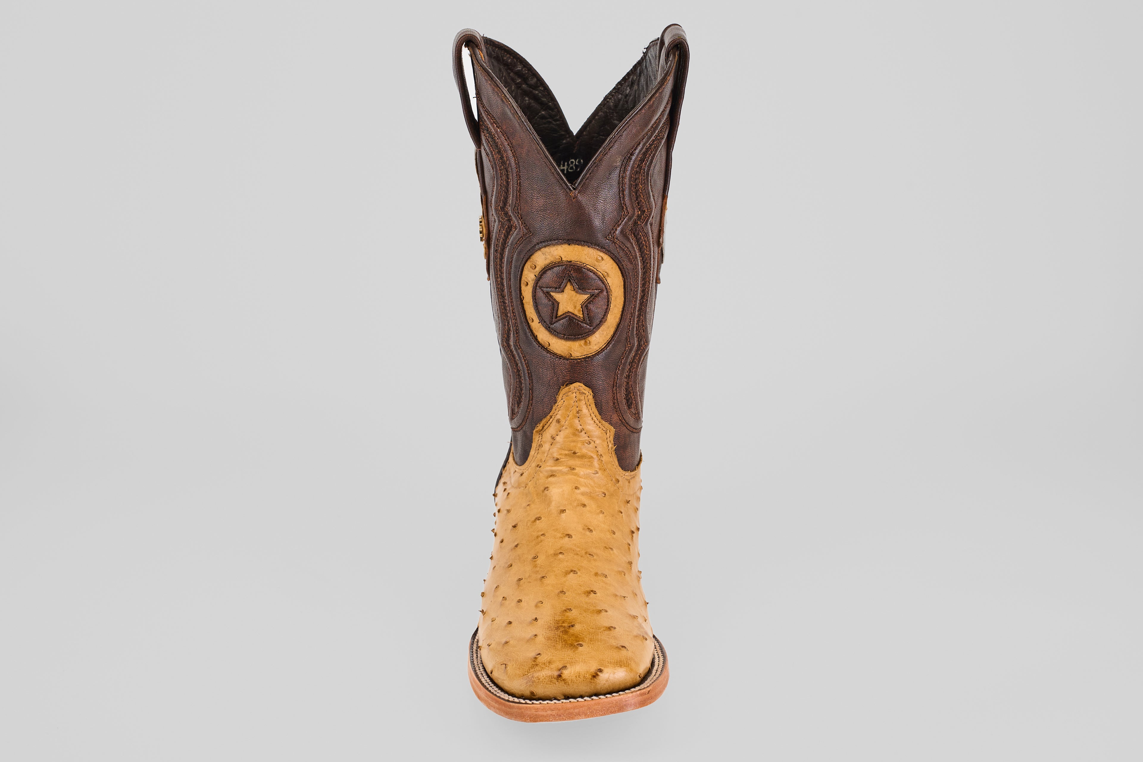 The Exotic Full Quilt Ostrich - Fawn - Square Toe boot features a tan ostrich foot, dark brown shaft, and a star emblem patch, offering timeless cowboy style with premium craftsmanship.