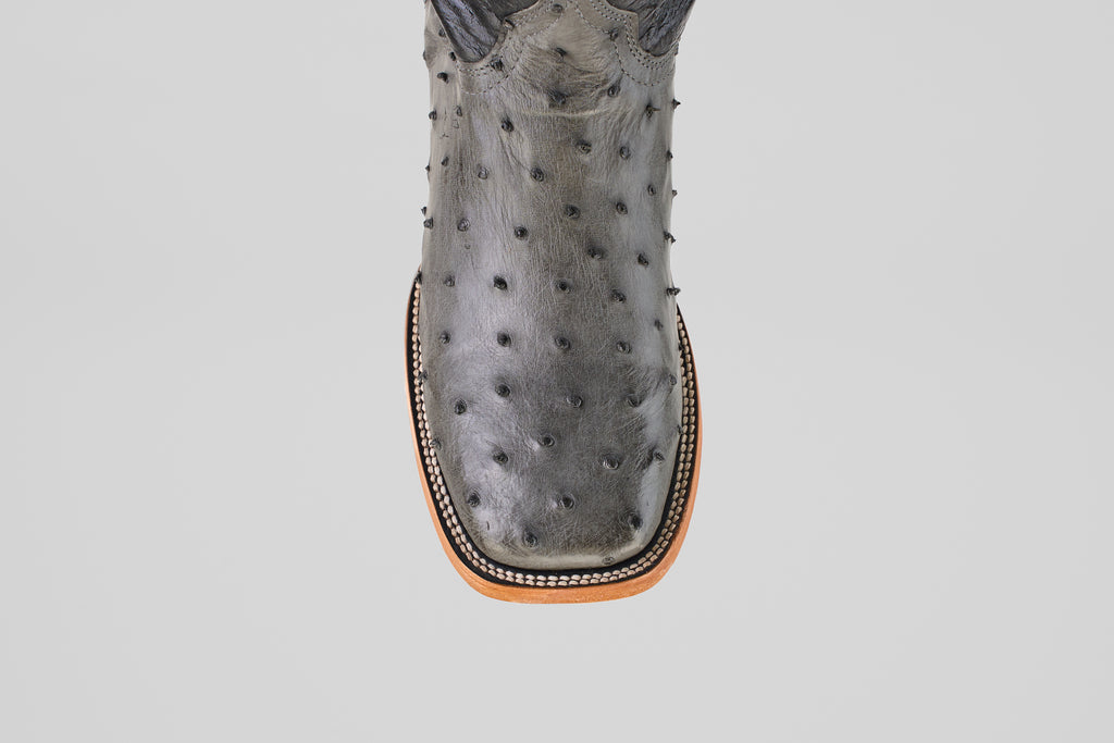 A close-up of the Exotic Full Quilt Ostrich - Gray - Square Toe boot, showing its gray full quilt ostrich leather, square tip, and decorative stitching along the sole's edge.