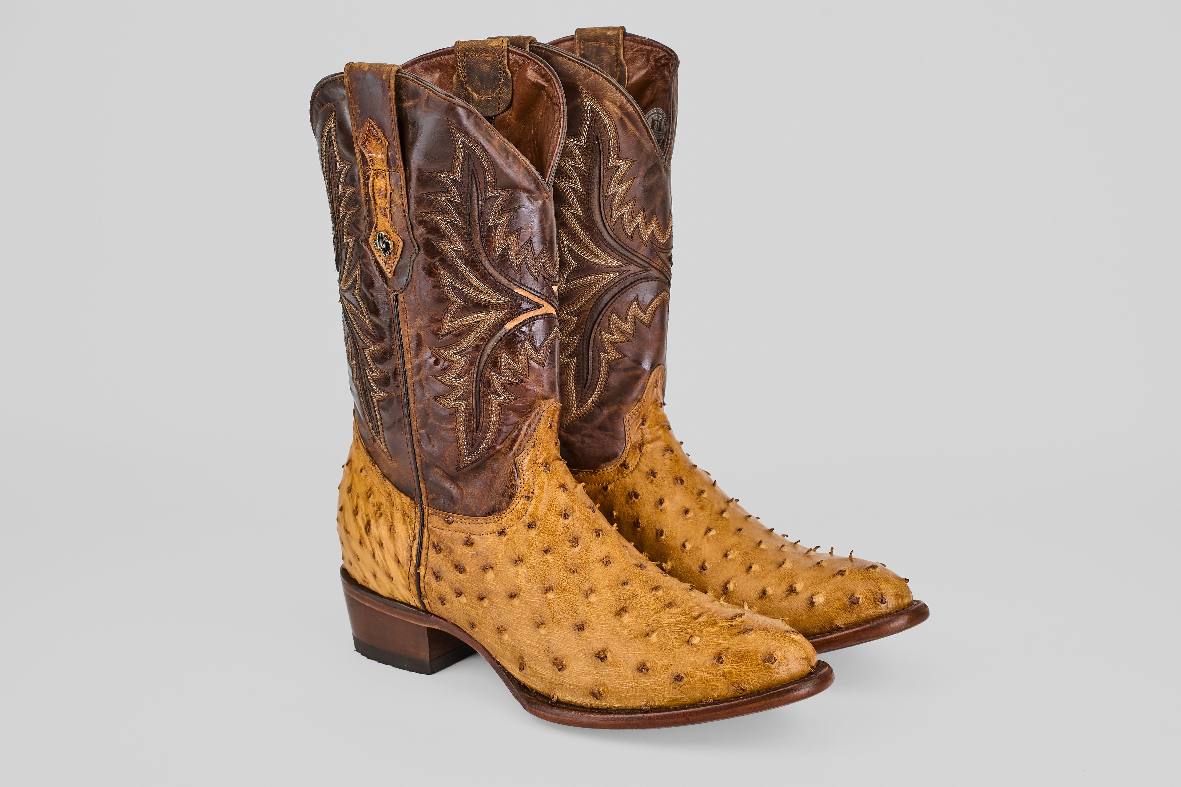 The Exotic Full Quilt Ostrich - Paja - Round Toe boots feature tan ostrich leather feet, brown shafts with decorative stitching, a round toe, low heel, and convenient pull straps for classic Western style.