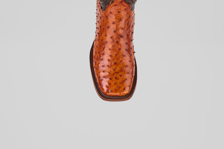A detailed close-up of the toe of the Austin - Brandy - Square Toe cowboy boot shows its rich, bumpy brown leather texture and square tip, set against a plain light gray background.