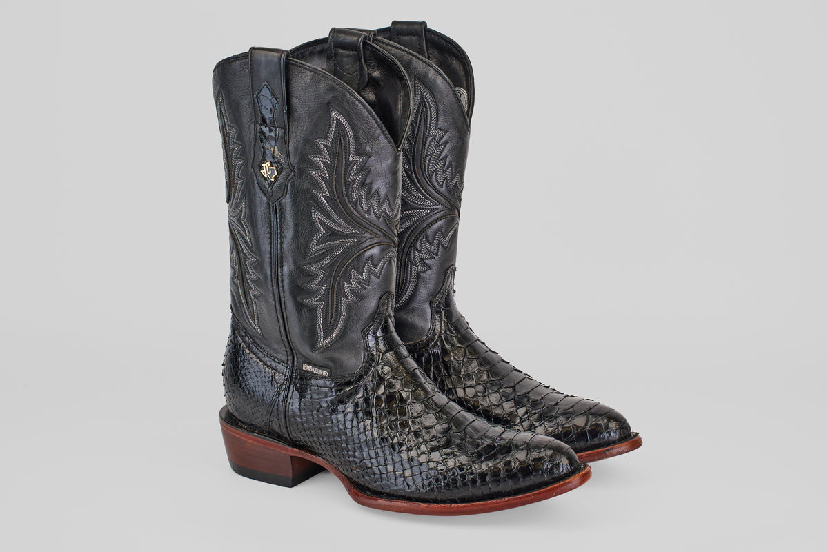 The Tanner - Black - Round Toe boots feature black leather with intricate shaft stitching, textured Python Negro Oval-patterned feet, brown wooden heels, and a decorative metal emblem on the side.