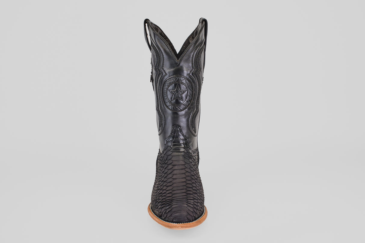 The Tanner – Matte Black – Roper Toe boot stands upright on a light brown sole, featuring a scaly texture and stitched star emblem on the shaft, showcasing western style against a clean white background.