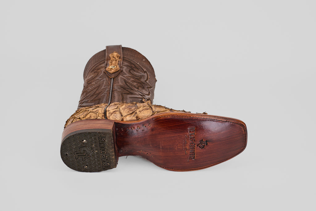 The Conor - Matte Orix - Narrow Square Toe features brown Pirarucu leather, detailed stitching, a textured lower section, and a square toe, displayed on its side to reveal the sole and heel against a plain grey background.
