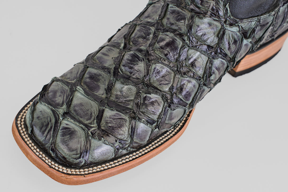 Close-up of the Conor - Charcoal - Square Toe boot, crafted in dark green and black reptile skin, features men's cowboy boots with a light wooden sole and detailed stitching.