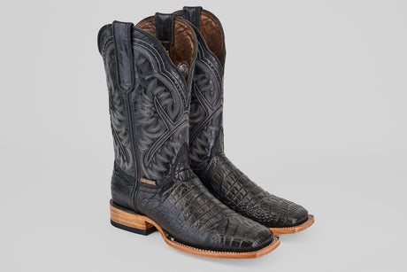 The Caiman Belly Black - Embossed Leather - Square Toe (E423) boots feature intricate stitching, a textured reptile-like pattern, light brown wooden soles, and square toes, displayed on a plain background.