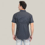 A man is standing with his back to the camera, wearing the Mens Performance Western Short Sleeve Aztec Print Navy Shirt (PGW10646) and light blue jeans against a plain light gray background.
