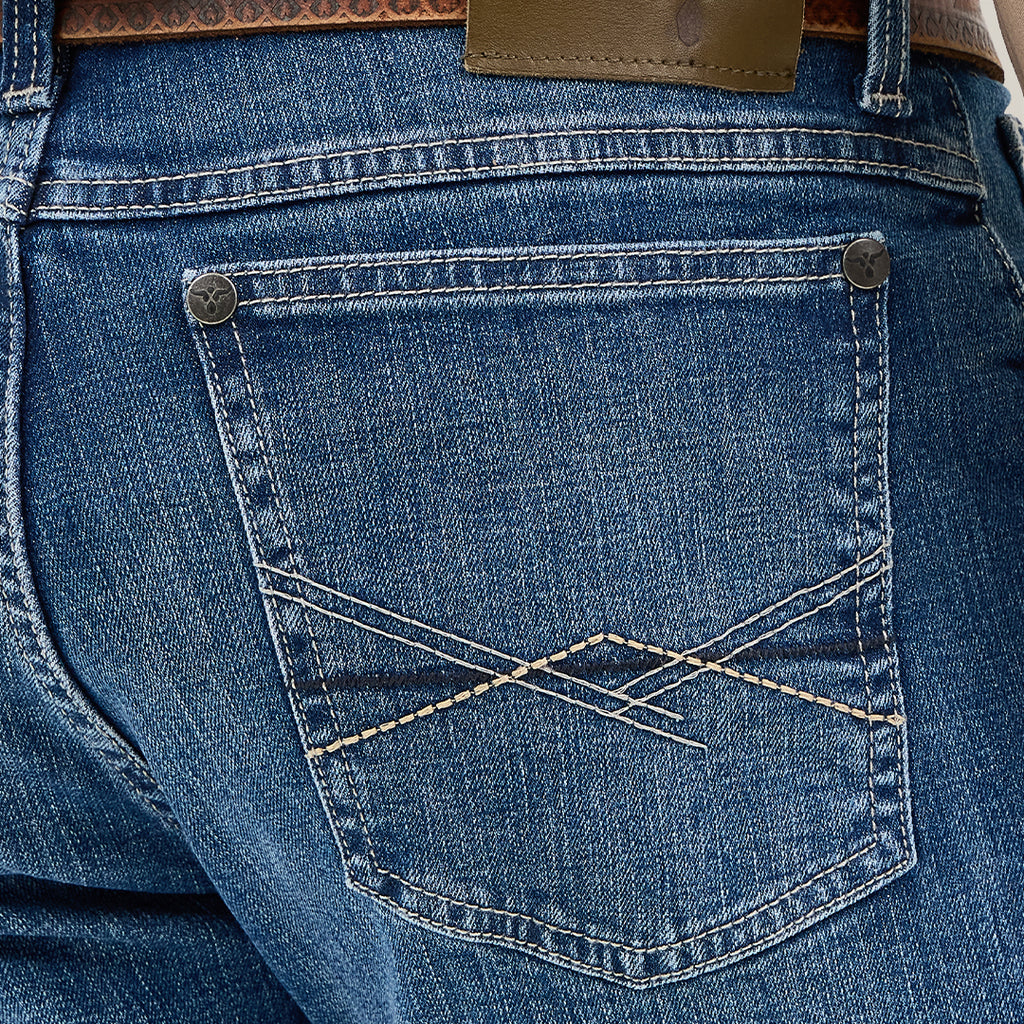 Close-up of a person wearing Mens Wrangler 20X No. 42 Vintage Bootcut Jeans, identifiable by their decorative stitching and Wrangler patch on the back pocket, secured with a brown patterned leather belt.